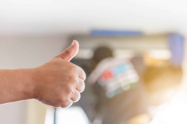 hand holding thumbs up in front of a technician repairing an ac unit