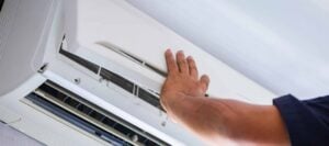Technician's hand reaching toward an open wall-mounted air conditioning unit during maintenance service in Louisiana.