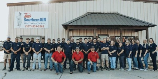 Large group of Southern Air Heating & Cooling employees in navy and red uniforms standing together in front of company building in Louisiana.