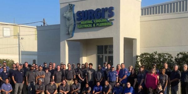 Large group of employees in uniforms standing in front of Surgers Heating, Cooling, Electrical & Plumbing storefront.
