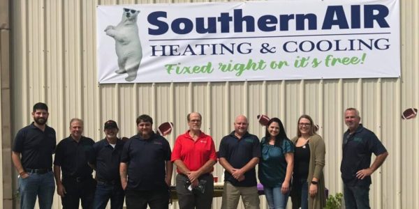 Southern Air team members standing in front of company sign with polar bear logo and motto 'Fixed right or it's free' in Port Allen.