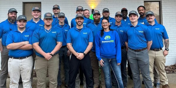 Professional team of HVAC and electrical technicians wearing blue Southern Air uniforms posing together in front of a brick building.